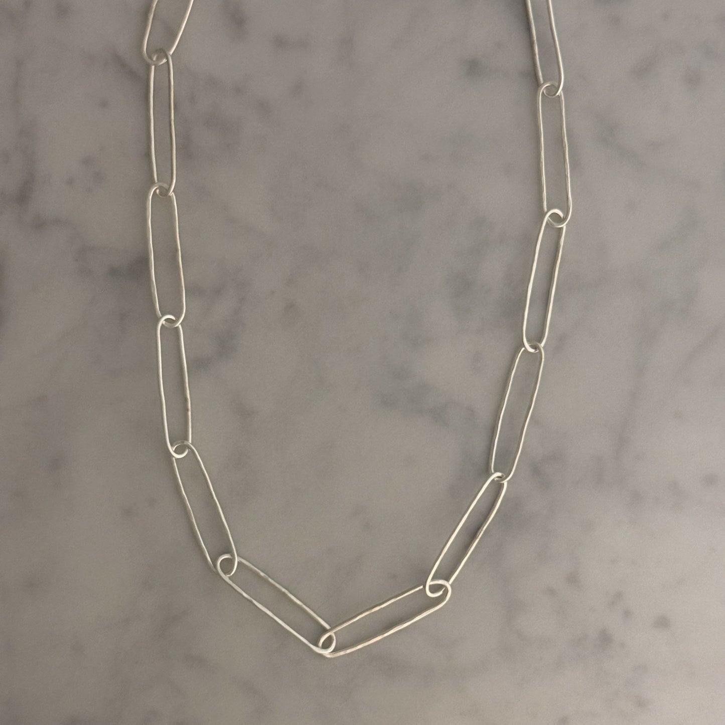 A silver paperclip chain necklace laid flat on a light gray and white marble surface.