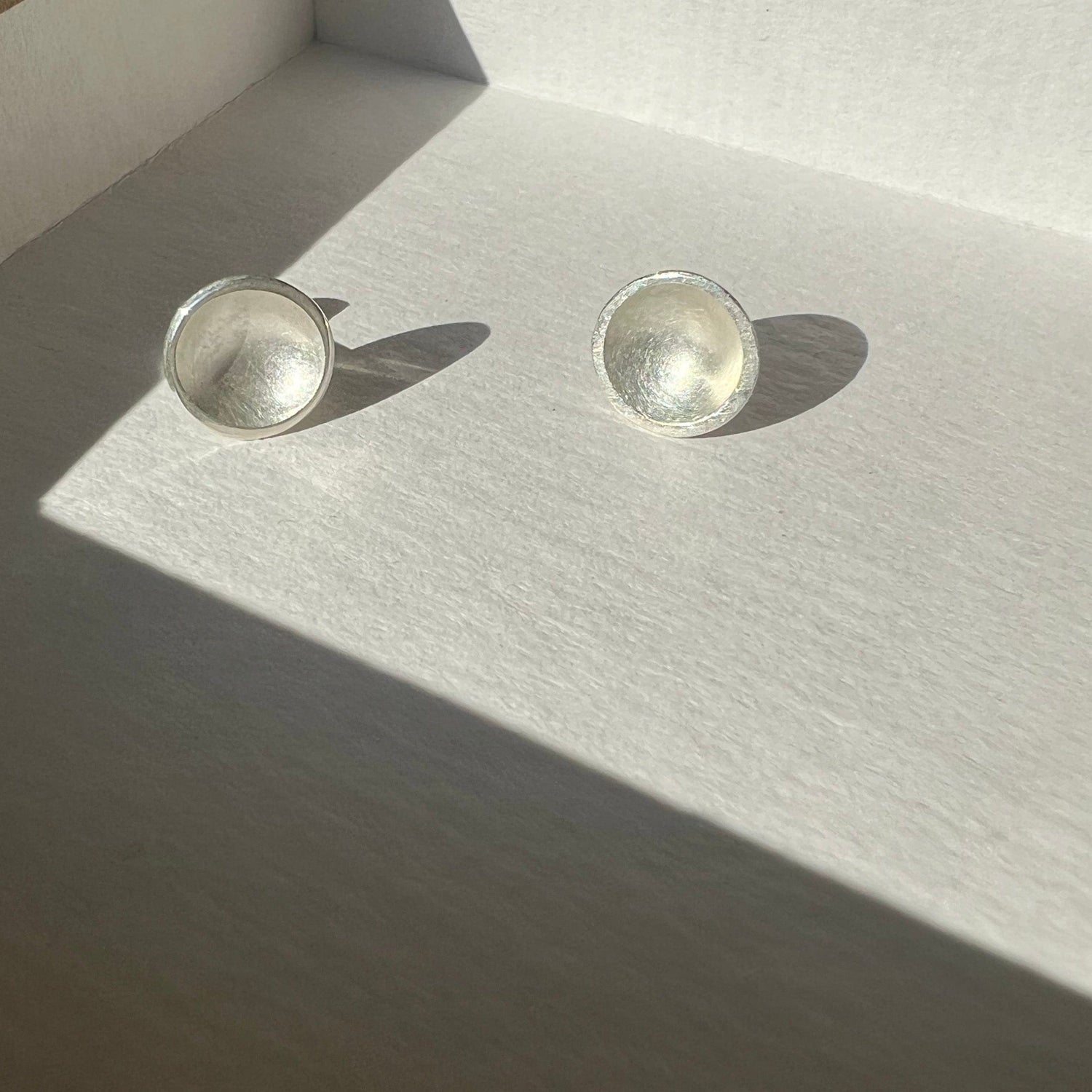 A pair of sterling silver post earrings with a bowl-shaped design, placed on a grey surface.