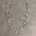 A silver paperclip chain necklace laid flat on a light gray and white marble surface.