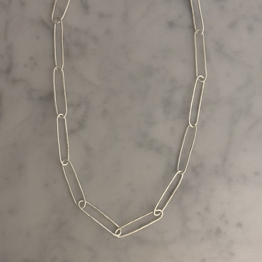 A silver paperclip chain necklace laid flat on a light gray and white marble surface.