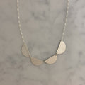 A silver necklace with three textured, semi-circular leaf-like drops hanging from a delicate silver chain, displayed on a light gray marble surface.