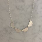 A silver necklace with three textured, semi-circular leaf-like drops hanging from a delicate silver chain, displayed on a light gray marble surface.