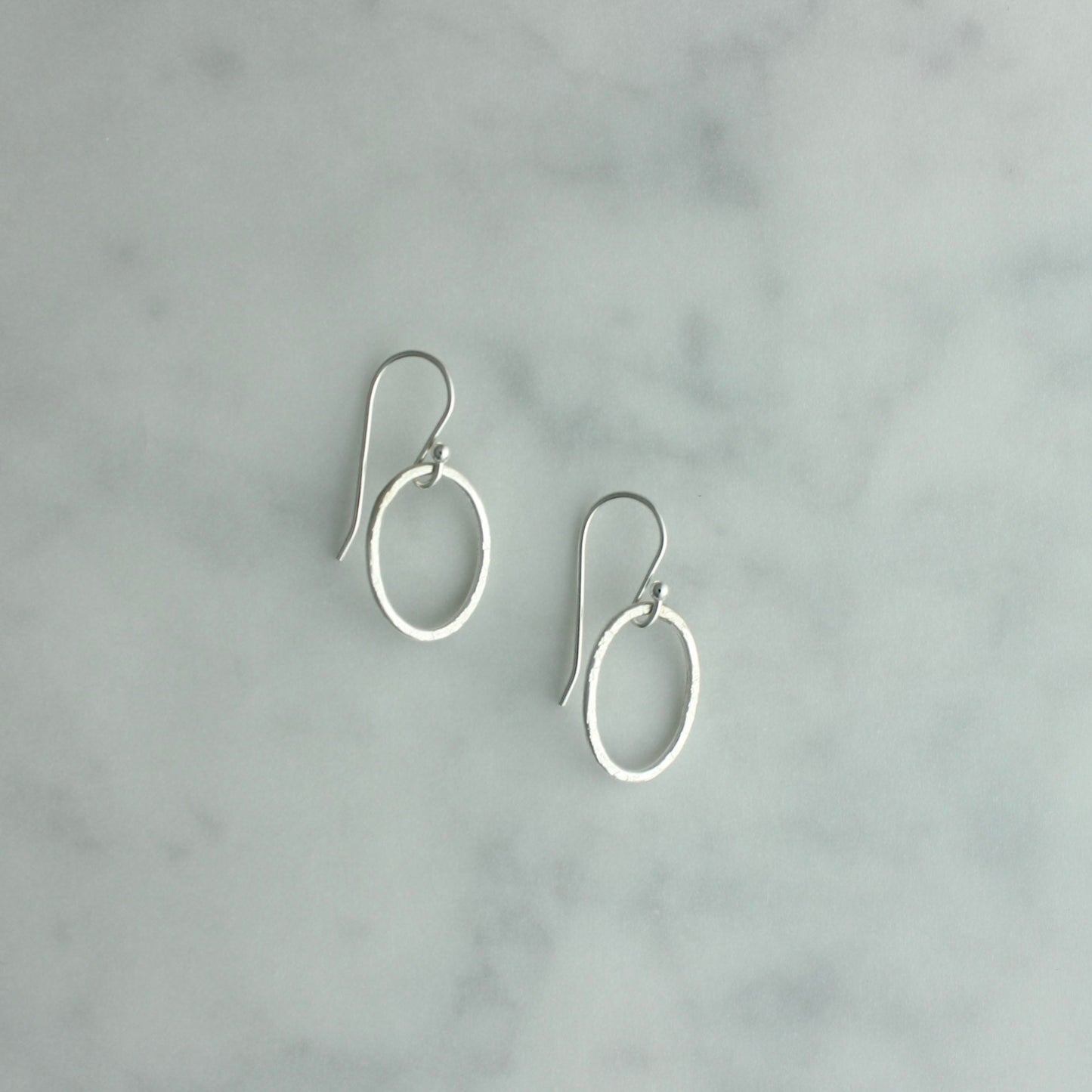 Pair of silver hoop earrings on a gray marble background