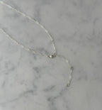 A delicate silver chain necklace with a lobster clasp and an extender chain featuring small round beads, displayed on a white and gray marble surface.
