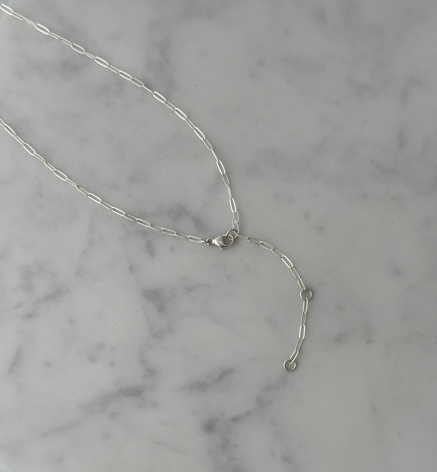 A delicate silver chain necklace with a lobster clasp and an extender chain featuring small round beads, displayed on a white and gray marble surface.