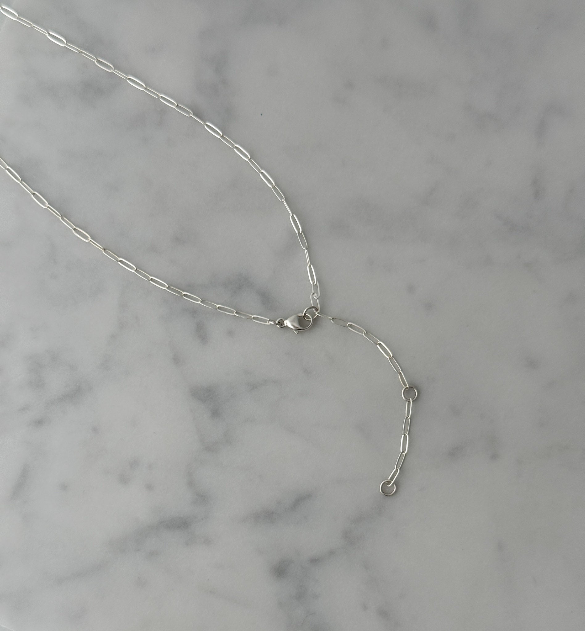 A delicate silver chain necklace with a lobster clasp and an extender chain featuring small round beads, displayed on a white and gray marble surface.