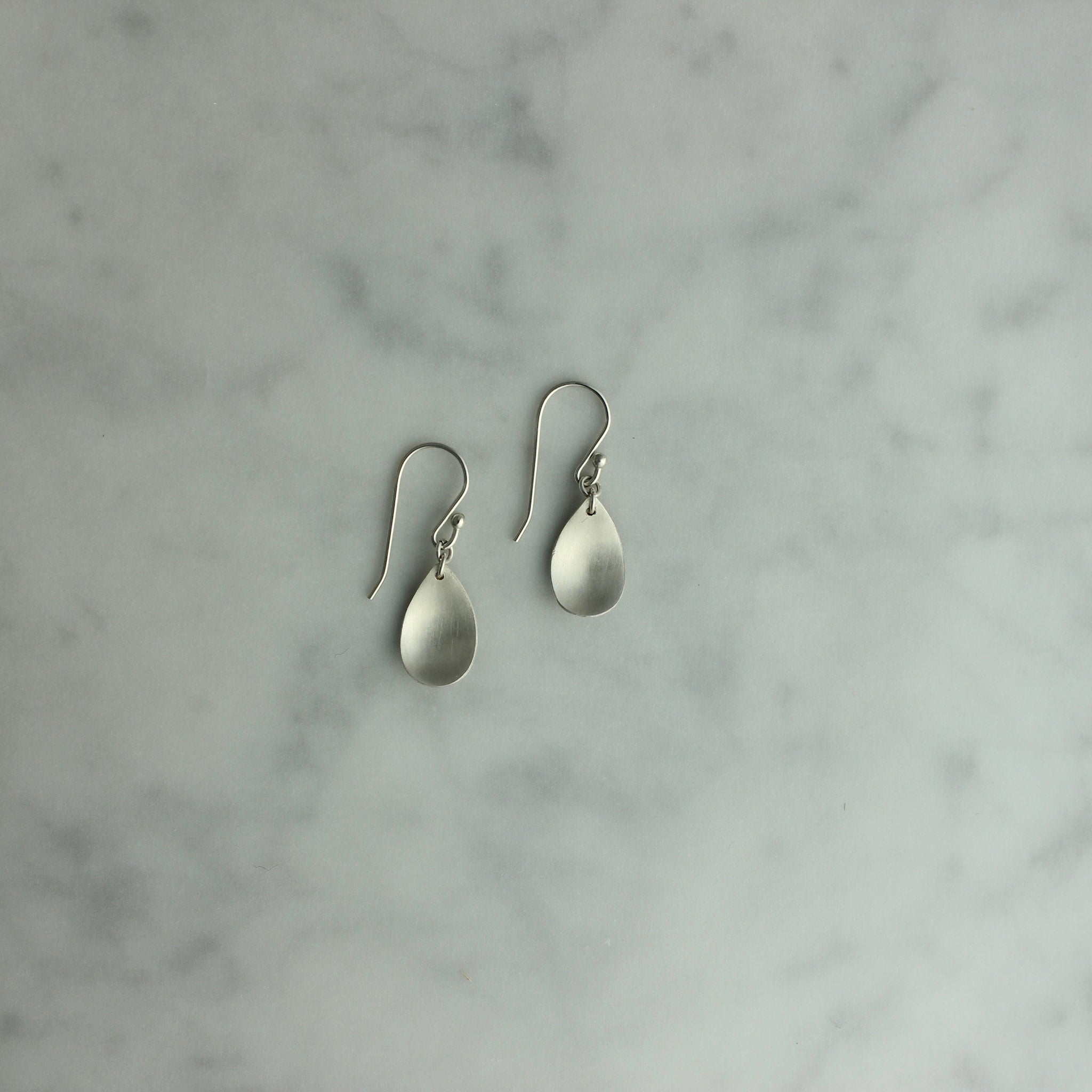 Pair of silver teardrop earrings on a marble surface