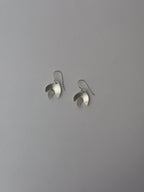A pair of silver-toned dangle earrings with a sculptural, layered petal-like design, shown against a plain gray background.