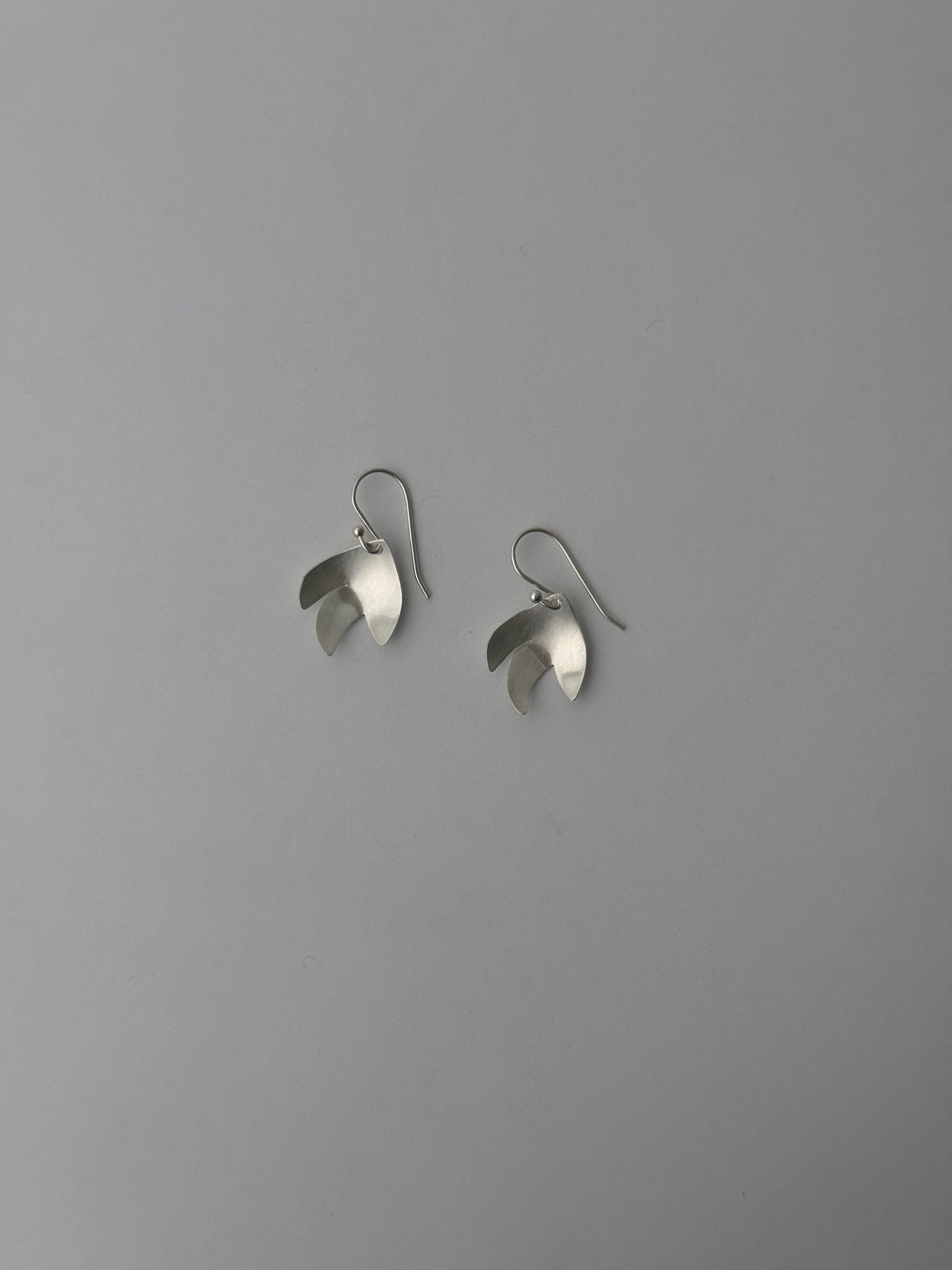 A pair of silver-toned dangle earrings with a sculptural, layered petal-like design, shown against a plain gray background.