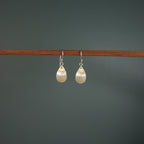 Pair of pearl earrings hanging on a wooden rod against a dark background