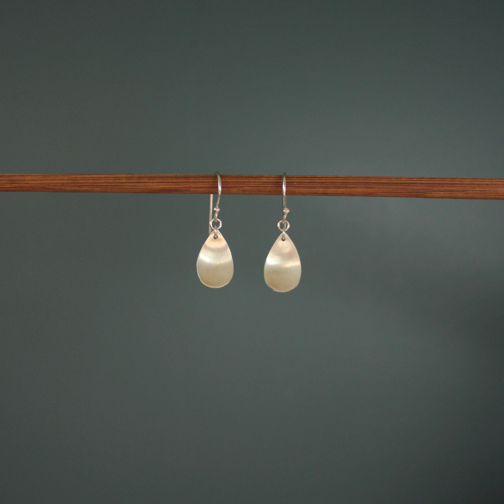Pair of pearl earrings hanging on a wooden rod against a dark background